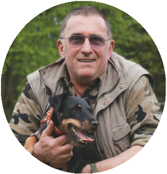 Ein Mann in einer Tarnjacke strahlt vor Freude im Freien und hält seinen treuen schwarz-braunen Hund im Arm. Diese herzerwärmende Szene unterstreicht die unausgesprochene Verbindung, einen wahren „Kontakt“, der über Worte hinausgeht. - Jagdhundeausbildung-Saar - Hundeschule für Jagdhunde, Prüfungsvorbereitung, Brauchbarkeit - Spieser Str. Hundeplatz am Sendeturm - 66299 Friedrichsthal